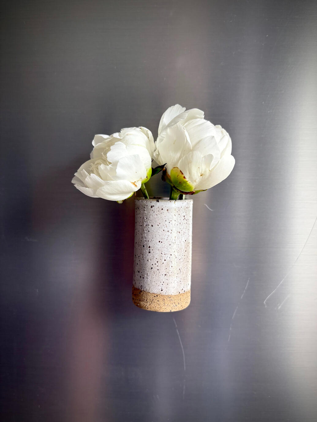 Each one is handmade from high-fire clay and finished with snow glaze. We’ve secured an extra-strong magnet on the back, so it stays put wherever you place it. The vase measures approximately 3” x 1.5” x 1.5”. You can purchase it on my etsy page!